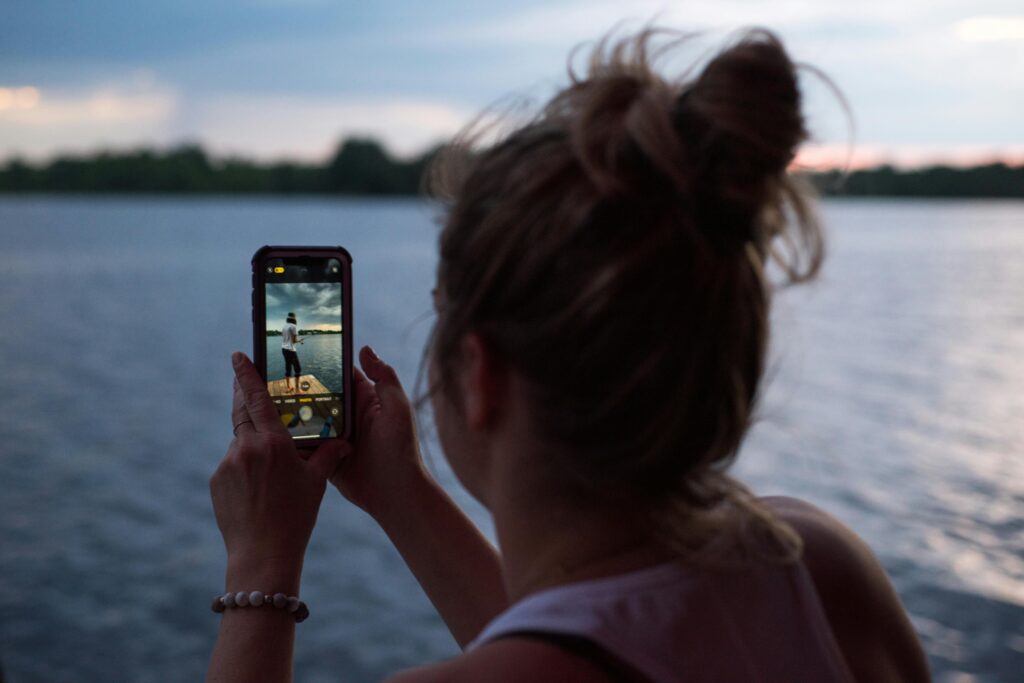 Person using a mobile phone by a lake, highlighting the need for a mobile signal booster to stay connected in weak network areas. by using this ultimate buying guide